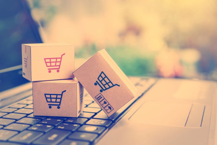 Paper cartons with a shopping cart or trolley logo on a laptop keyboard, depicts customers order things from retailer sites via the internet.