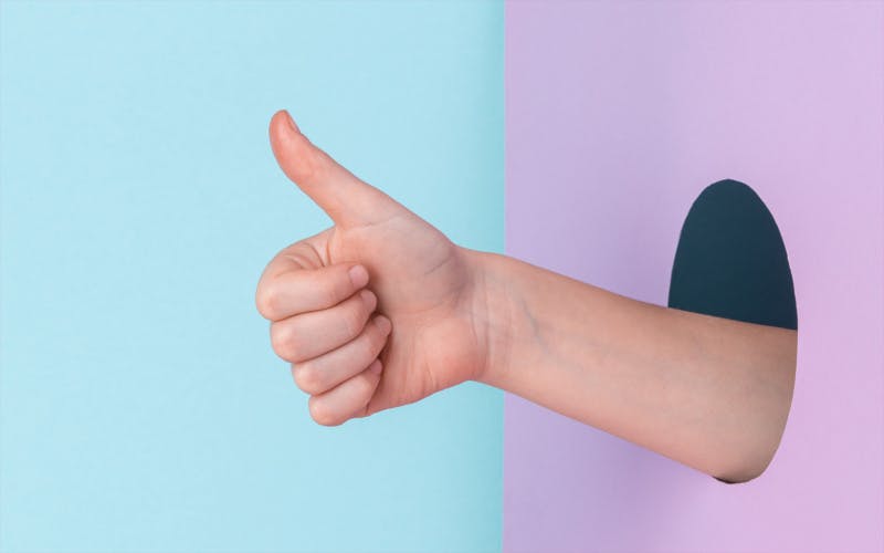 thumbs up emerging from circular hole in pink wall