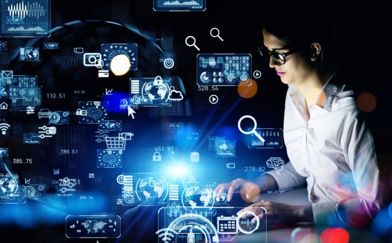 Photograph of a young woman typing as if on a keyboard, surrounded by holographic imagery of icons like a shopping cart, wi-fi symbols, a magnifying glass, a globe, etc.